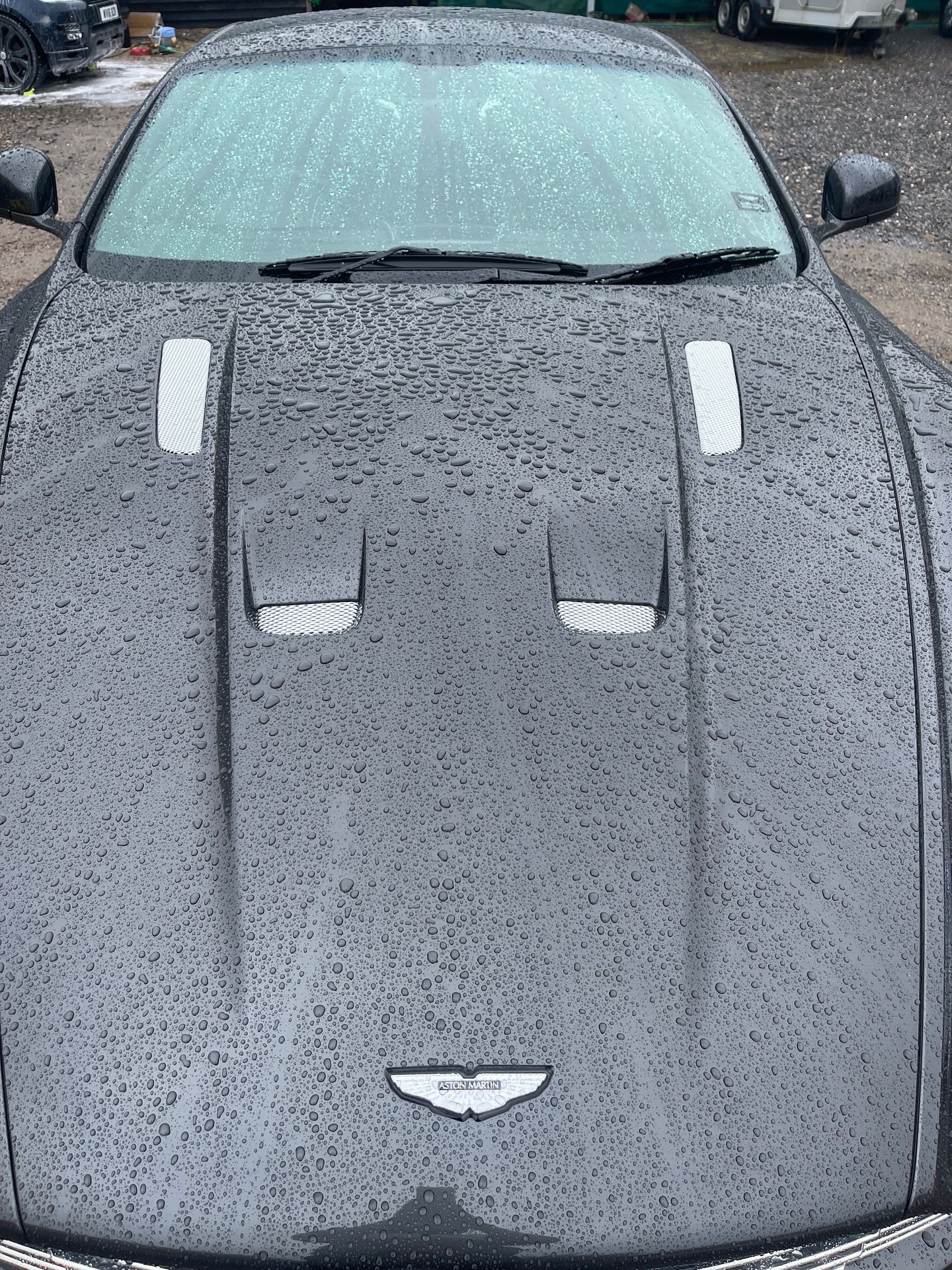 Raindrops on the hood of a sleek black car with a metallic logo.
